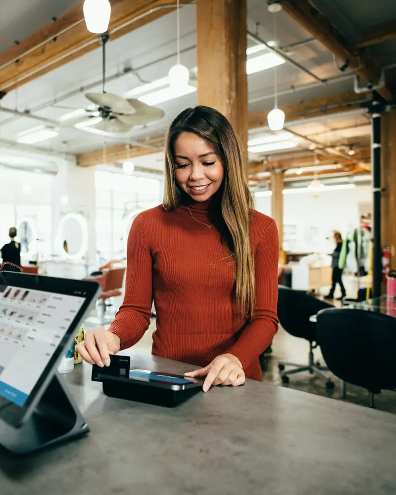 Smiling business owner serving a customer at the shop counter using a tablet till
